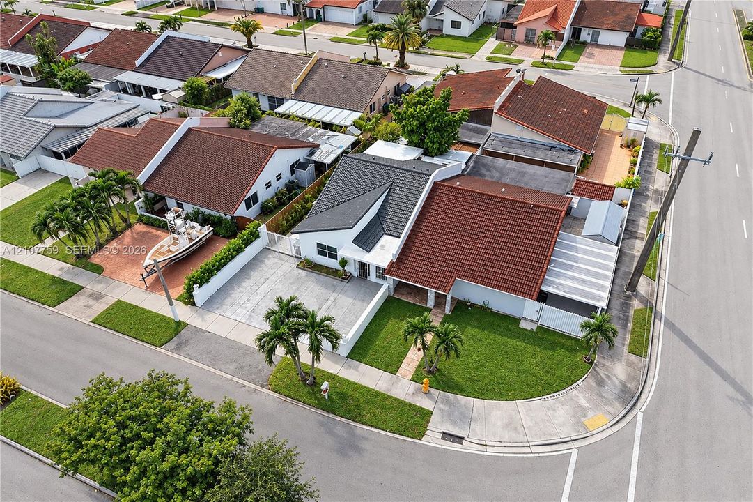 Corner-lot property featuring a multi-level tile roof, paved driveway, enclosed perimeter wall, and manicured lawn with mature palm trees