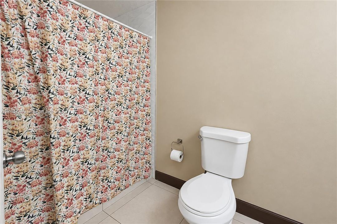 Bathroom featuring a white ceramic toilet, tiled flooring, and a wall-mounted metal toilet paper holder