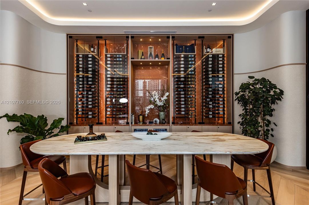 Custom built-in glass-front wine display with integrated accent lighting and natural stone-finish back panel, featuring curved wall detailing and chevron-pattern wood-finish flooring