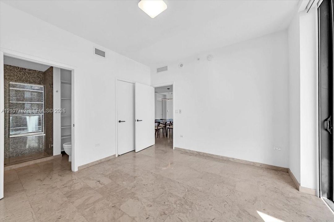 Interior room featuring large-format stone tile flooring, neutral wall finishes, solid-core interior doors with matte black hardware, and an attached bathroom with tiled wall accents