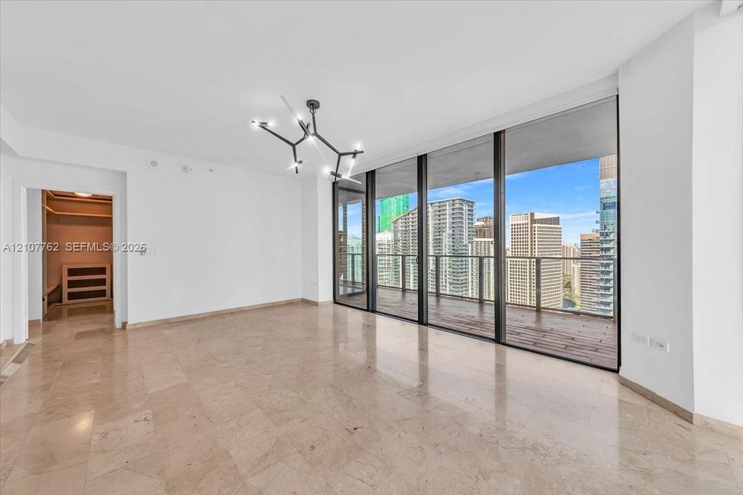 Floor-to-ceiling glass doors, stone tile flooring, private balcony with wood-finish decking, modern geometric chandelier, and built-in closet storage