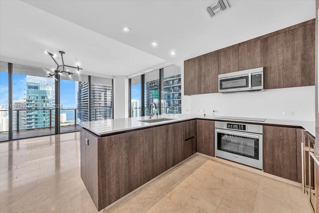 Kitchen featuring wood-finish cabinetry, stone countertops, stainless steel appliances, tile flooring, and floor-to-ceiling windows