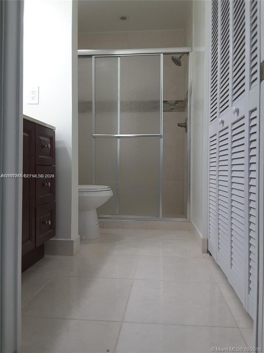 Bathroom featuring a glass-enclosed shower, dark wood-finish cabinetry, louvered closet doors, and tile flooring