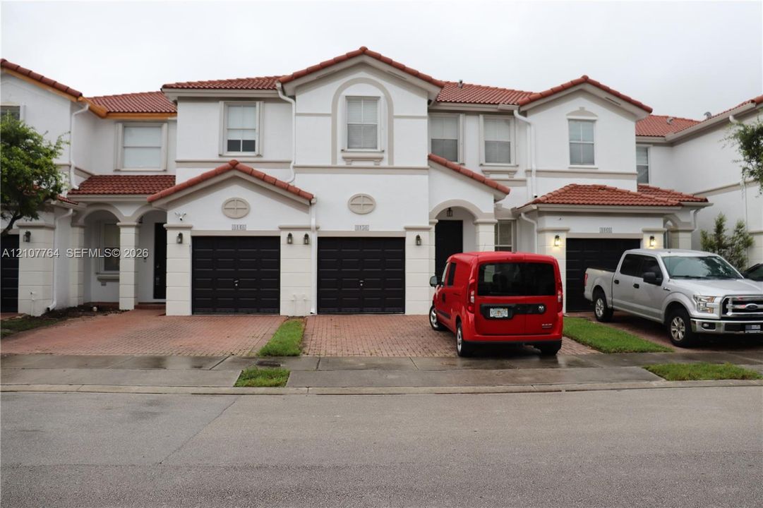 Mediterranean-inspired exterior featuring a multi-gabled tile roof, stucco facade, decorative arched detailing, and integrated multi-car garages with brick-paver driveways