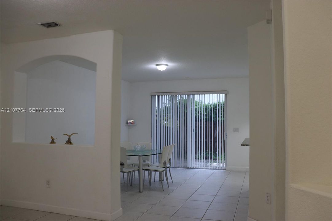 Interior featuring arched wall niche, neutral tile flooring, and sliding glass doors with vertical blinds
