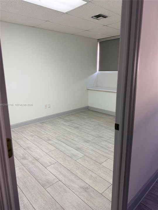 Room featuring wood-finish tile flooring, neutral wall tones, a built-in window ledge, and a drop ceiling