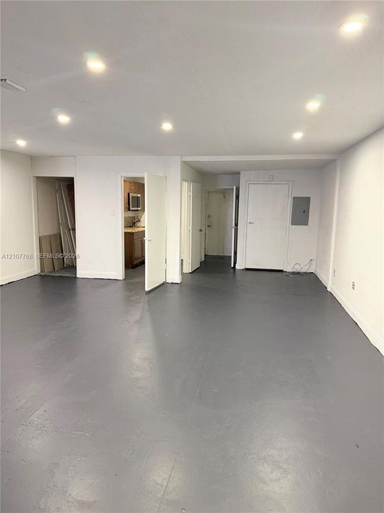 Open-concept interior featuring smooth grey-painted concrete flooring, recessed ceiling lighting, and multiple access doors