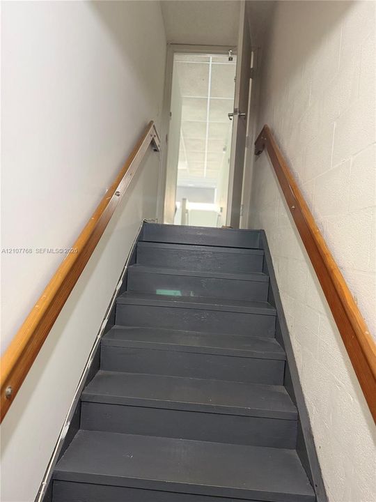 Staircase featuring dark-finished treads and dual natural wood handrails mounted on painted block walls