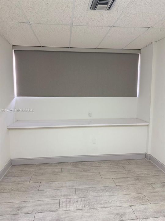 Built-in desk with a solid surface countertop, tile flooring with a wood finish, and neutral window shades