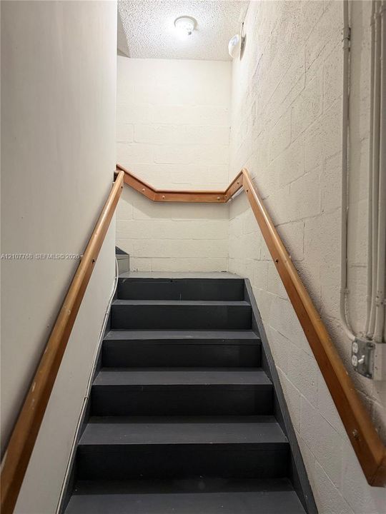 Staircase featuring dark painted treads and mounted natural wood handrails against painted masonry walls