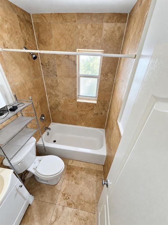 Bathroom featuring full-height natural stone tile surround, integrated soaking tub, stone tile flooring, and a single-hung window
