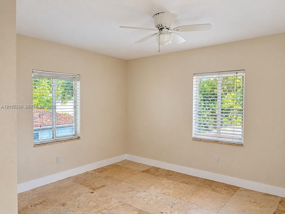 Interior room featuring natural stone tile flooring, two windows with installed horizontal blinds, and a white ceiling fan with an integrated light fixture
