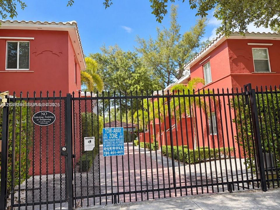 Gated residential complex featuring vibrant stucco exterior walls, a terracotta-style tile roof, and a paved brick driveway