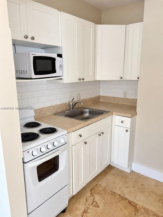 Kitchen featuring white Shaker-style cabinetry, a white subway tile backsplash, solid-surface countertops, an integrated stainless steel sink with a high-arch faucet, and white electric range