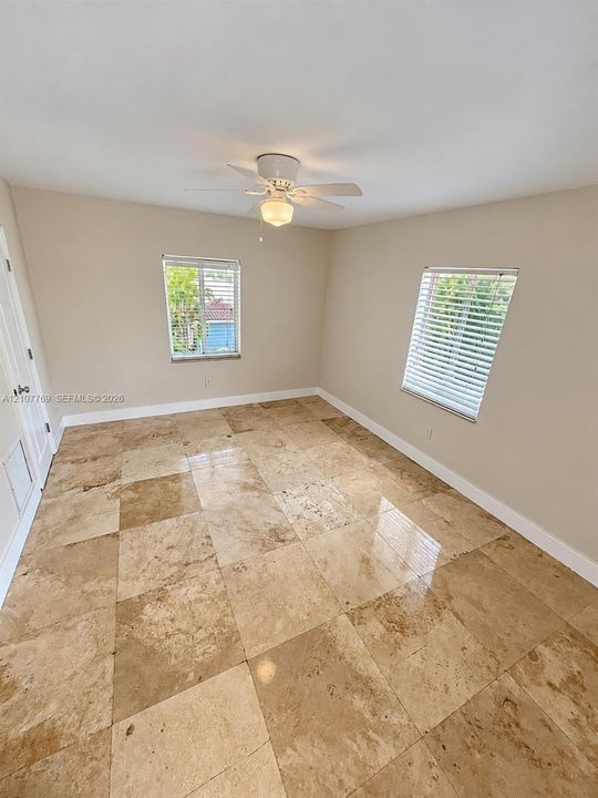 Interior space featuring large-format tile flooring, dual windows with horizontal blinds, and a white ceiling fan with integrated lighting