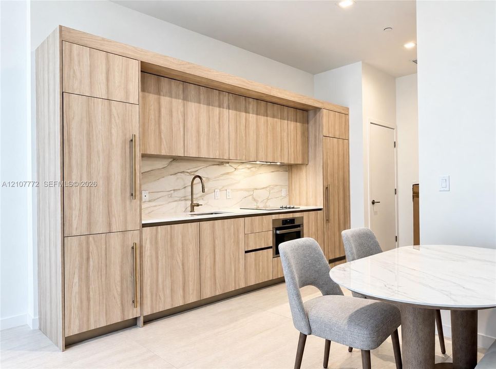 Modern kitchen featuring wood-finish cabinetry with integrated appliances, light-toned stone-style backsplash, undermount sink with a metallic pull-down faucet, and built-in cooktop and oven