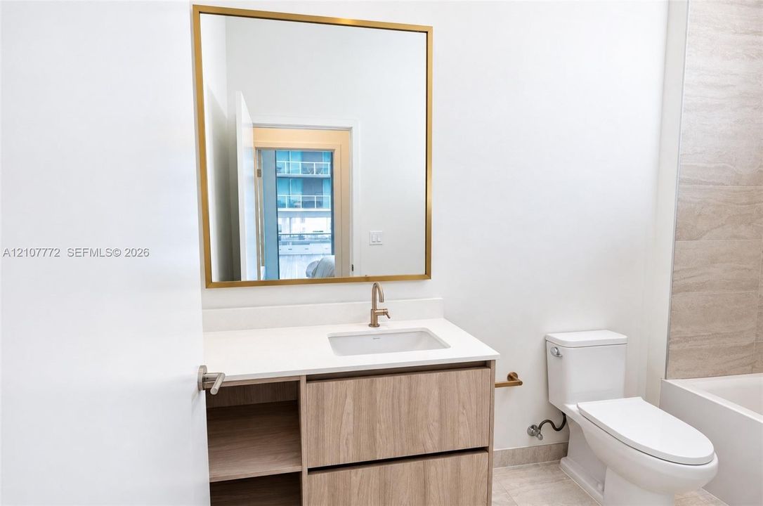 Bathroom featuring a vanity with wood-finish cabinetry, white countertop with an integrated basin, gold-toned hardware, and a square wall mirror with a metallic frame