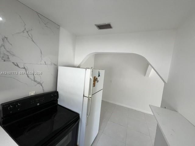 Kitchen featuring large-format wall tiling with a veined pattern, smooth-top electric range, and a decorative arched architectural opening
