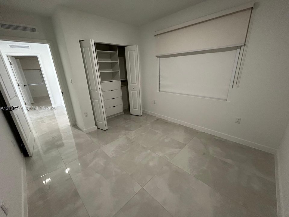 Large-format polished tile flooring, built-in closet system with integrated shelving and drawers, neutral interior walls, and multi-panel doors