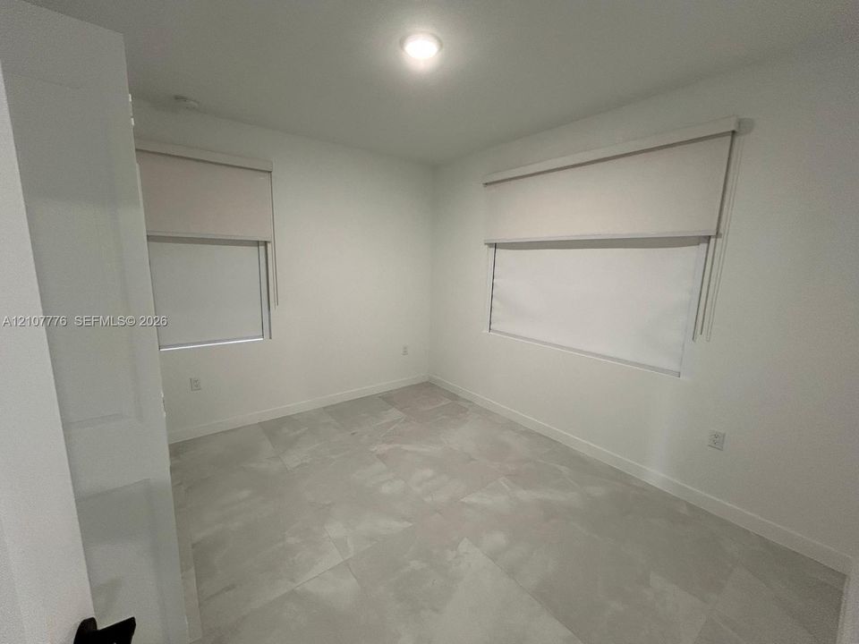 Neutral interior featuring large-format tile flooring, crisp white walls, and dual windows equipped with roller shades