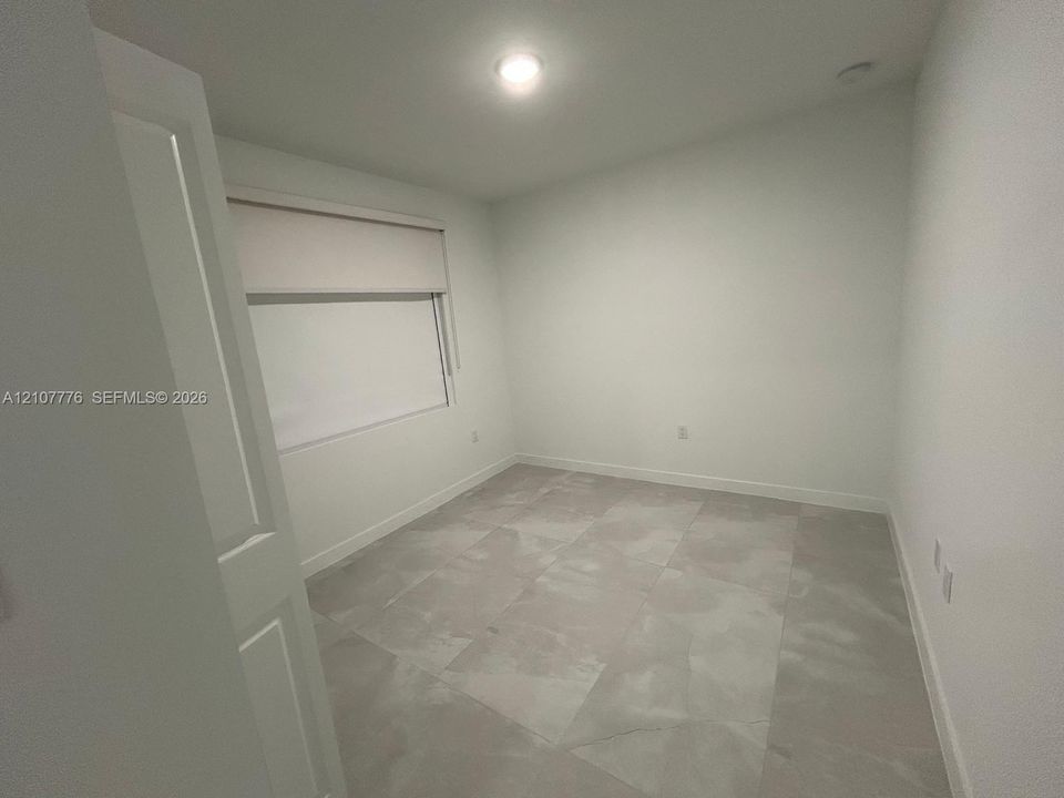Neutral-toned room featuring large-format tile flooring, crisp white walls, and a recessed ceiling light fixture