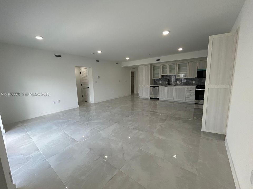 Large-format tile flooring, recessed ceiling lighting, light-toned cabinetry with glass-front uppers, and stainless-steel appliances