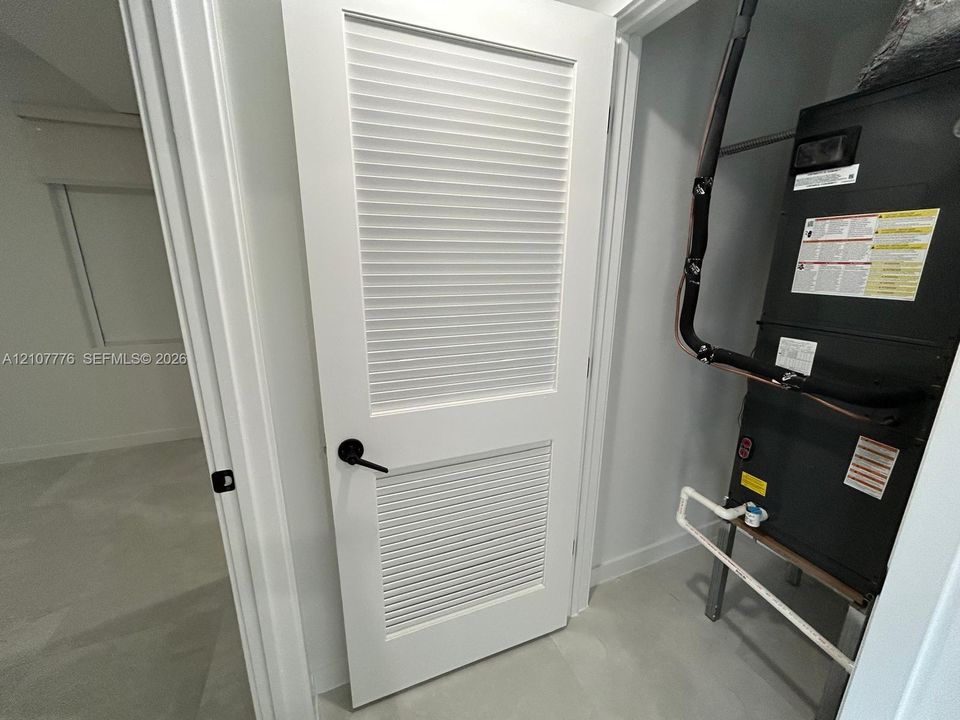 Utility closet featuring a white louvered door with matte black hardware and an installed mechanical furnace unit