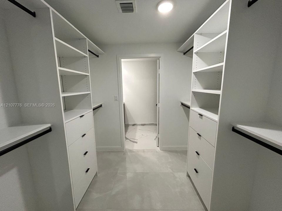 Walk-in closet featuring white built-in shelving, integrated dresser drawers with matte black hardware, and large-format tile flooring