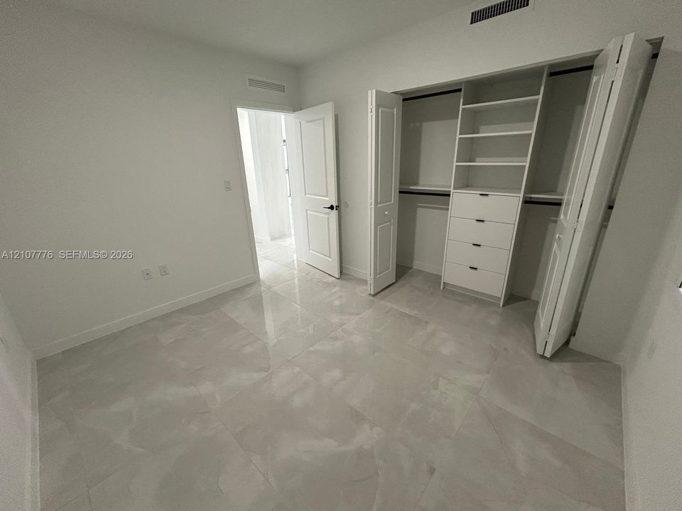 Room featuring large-format tile flooring, a custom walk-in closet with built-in shelving and drawers, and panel-style interior doors