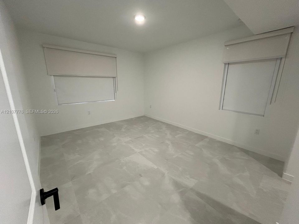 Neutral-toned interior room featuring large-format tile flooring, recessed ceiling lighting, and two windows equipped with roller shades