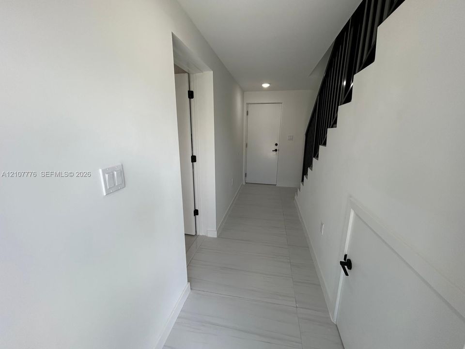 Entryway featuring large-format ceramic tile flooring, a staircase with matte black metal railings, and a solid-panel door with matching matte black hardware