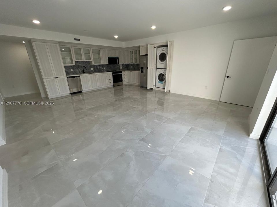 Large-format tile flooring, white cabinetry with integrated upper glass-front displays, stone-finish backsplash, stainless steel appliances, and built-in stacked laundry