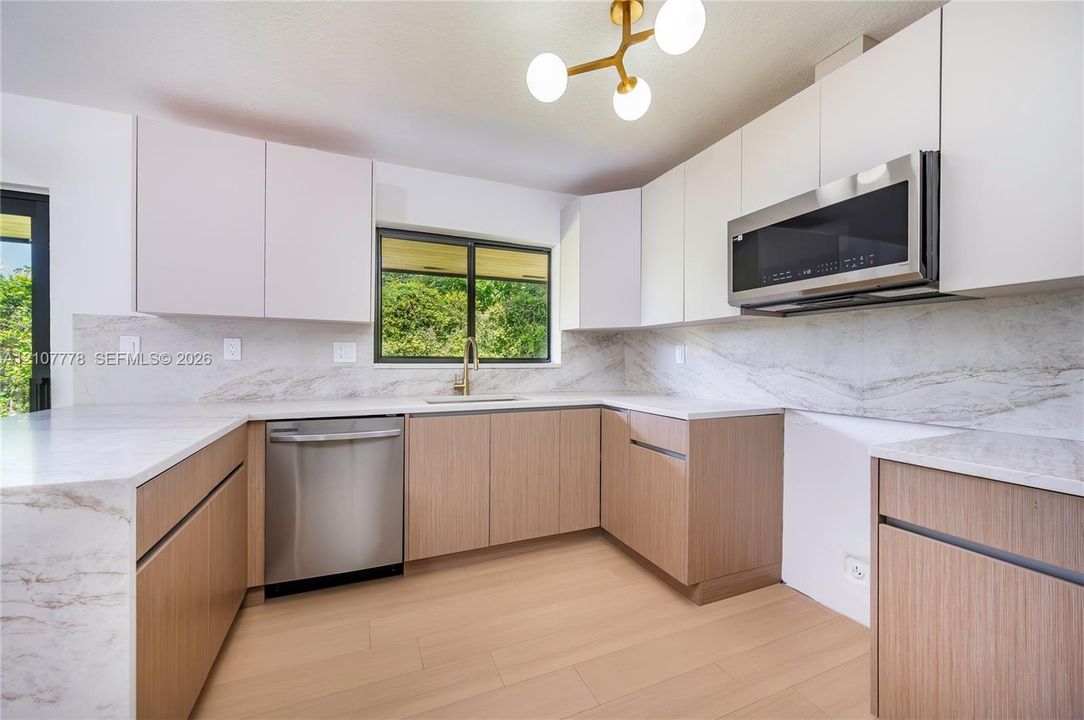 Kitchen featuring two-tone cabinetry with wood-finish lower units and solid-color upper units, stone-finish countertops and full-height backsplash, stainless steel appliances, wood-finish flooring, and multi-light chandelier