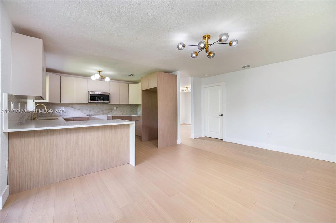 Kitchen featuring flat-panel cabinetry, quartz countertops, wood-finish flooring, gold-tone hardware, and a multi-bulb geometric light fixture
