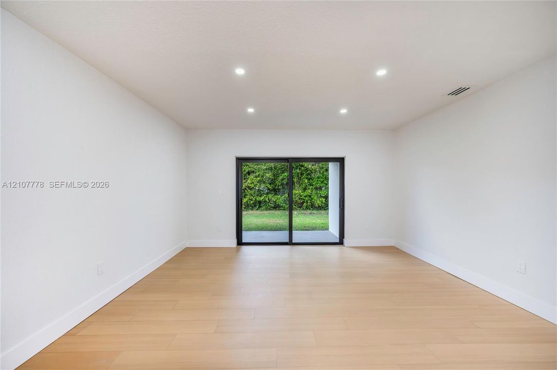 Interior space featuring light-toned wood-finish flooring, recessed ceiling lighting, and sliding glass doors with exterior access to a lawn area