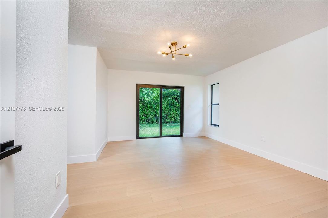 Interior space featuring wood-finish flooring, white walls, a multi-arm brass light fixture, and sliding glass doors