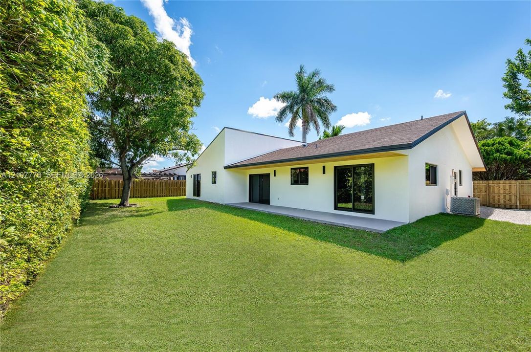 Exterior featuring a white stucco facade, expansive backyard lawn, concrete patio, sliding glass doors, and privacy fencing