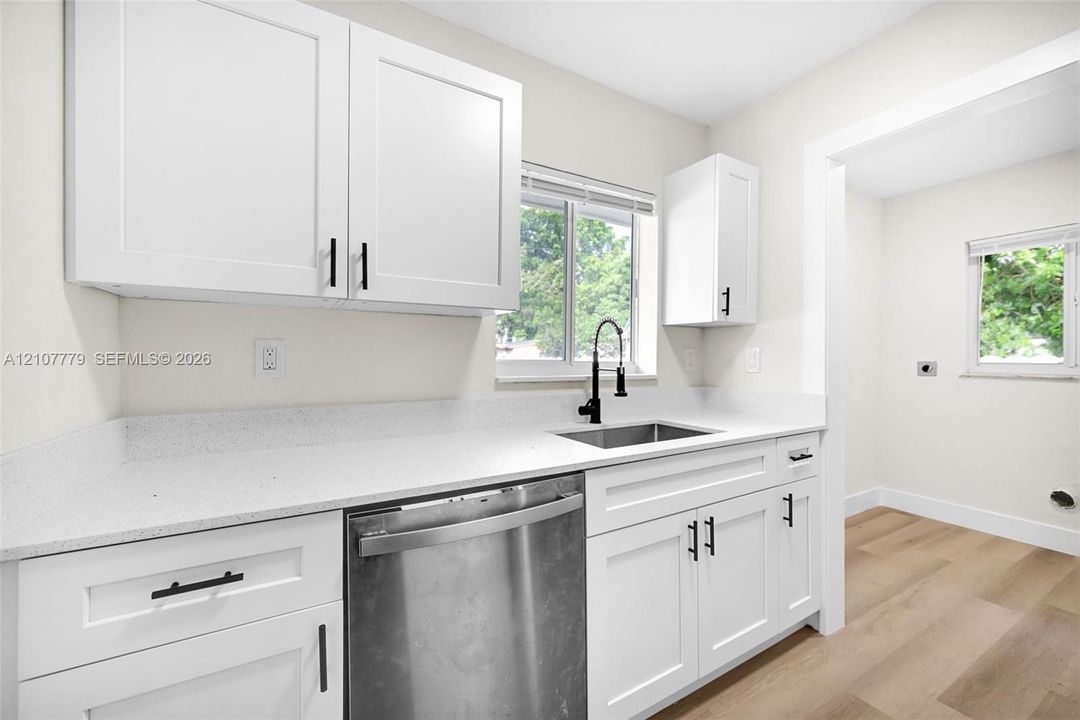 Kitchen featuring white Shaker-style cabinetry, matte black hardware, stone-composite countertops, stainless steel dishwasher, and a high-arc pull-down faucet