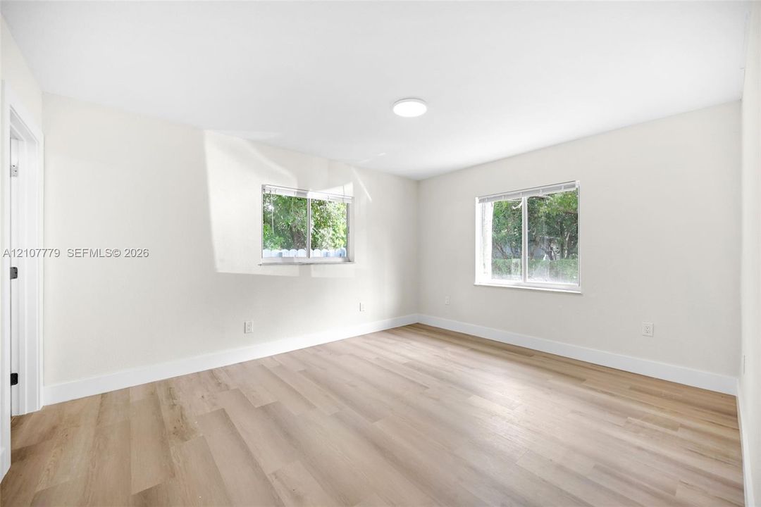 Neutral-toned interior space featuring wood-finish flooring, crisp white walls, and two dual-pane windows with horizontal blinds