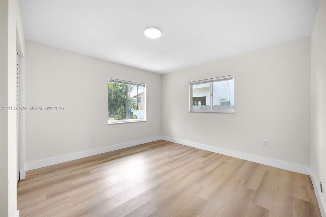 Neutral-toned interior featuring wood-finish flooring, dual windows with blinds, and a flush-mount ceiling light fixture