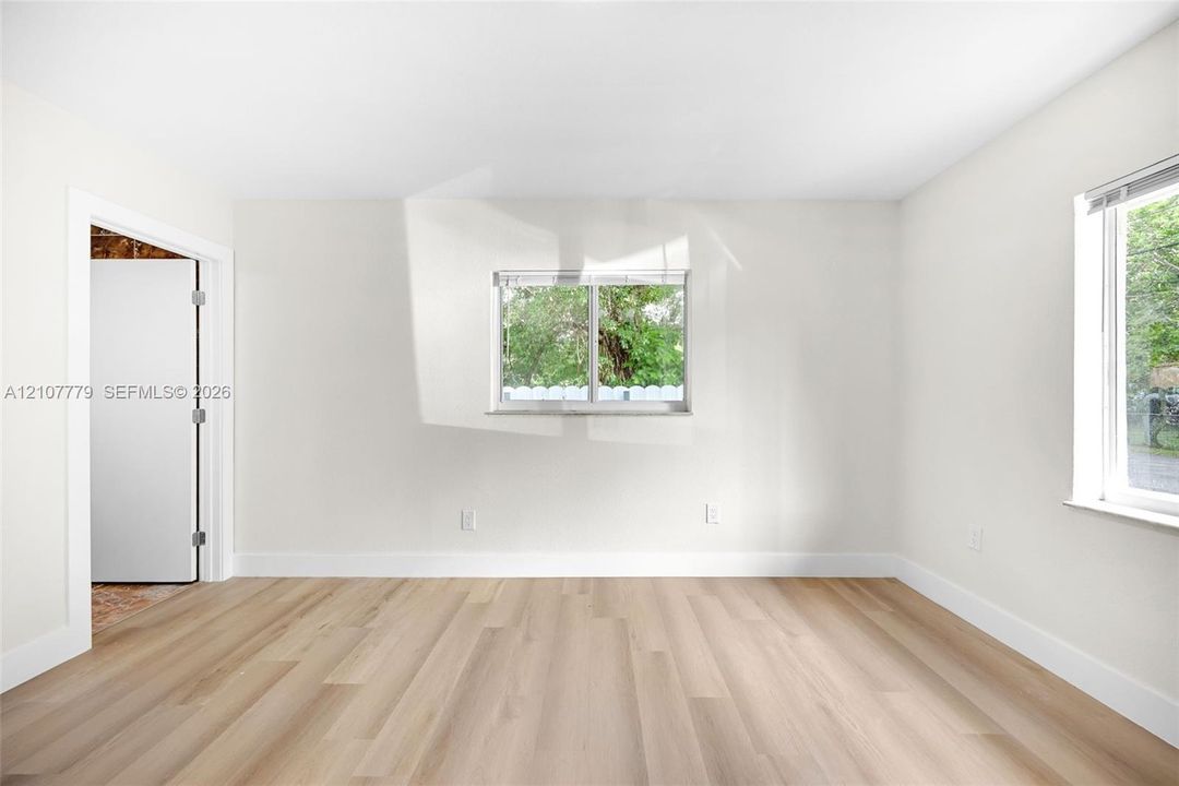 Neutral-toned interior room featuring wood-finish flooring, two sliding windows, and a doorway with a neutral-finished door