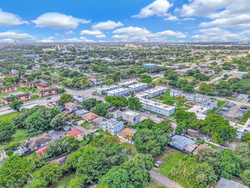 Aerial perspective of a multi-structure residential complex featuring low-rise flat-roof buildings, paved parking areas, and mature landscaping within a suburban environment