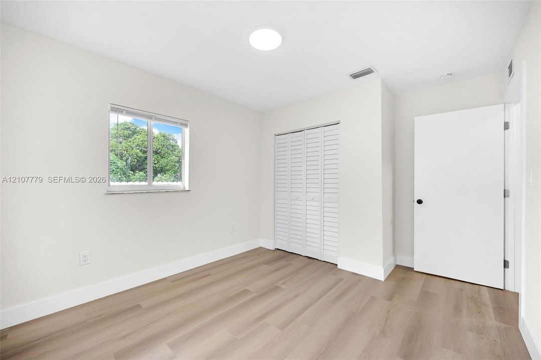 Neutral interior space featuring wood-finish flooring, a double-panel louvered closet door, a single-hung window with white blinds, and recessed lighting