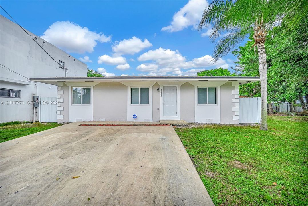 Single-story exterior featuring a light-toned smooth finish, quoined corner detailing, a central entry door, and a concrete driveway