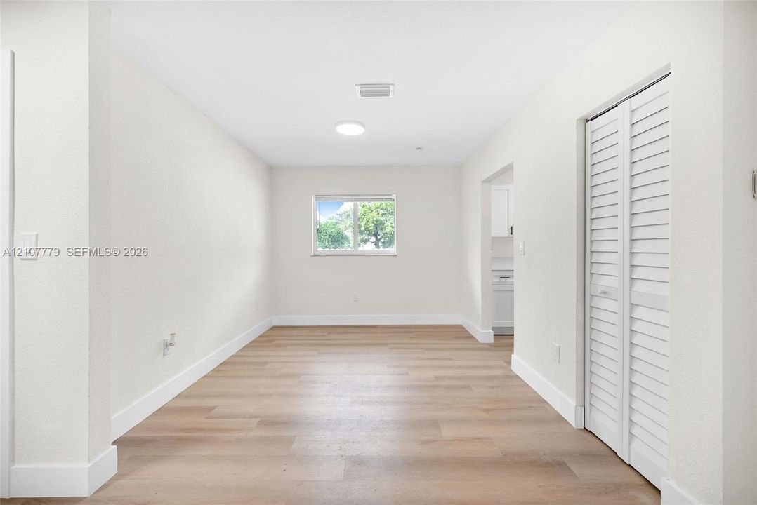 Interior space featuring wood-finish flooring, white walls, a single-pane window, a circular ceiling-mounted light fixture, and a white bifold closet door