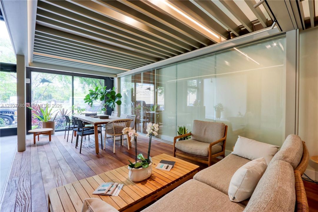 Covered patio featuring wood-finish flooring, a louvered metal ceiling, floor-to-ceiling glass wall panels, and structural support pillars