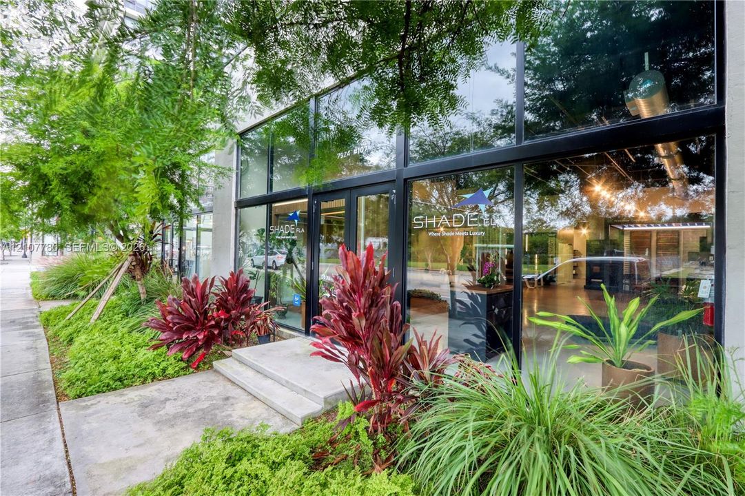 Floor-to-ceiling glass storefront, metal-framed window system, concrete entryway steps, and professional exterior landscaping