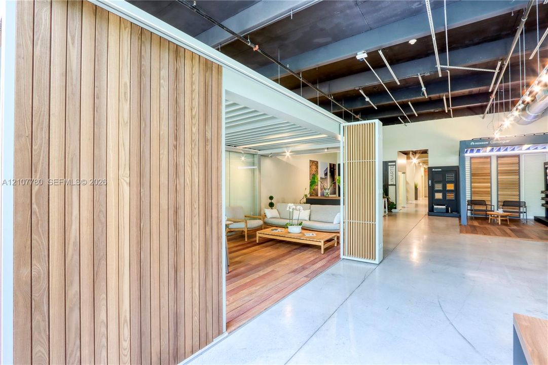 Industrial-style interior featuring exposed ceiling joists, polished concrete flooring, wood-panel wall treatments, and a retractable slatted privacy screen