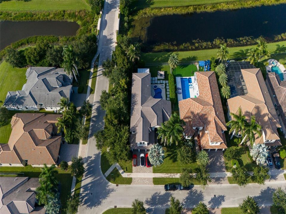 Aerial perspective of a property featuring a swimming pool, attached spa, paver driveway, and mature palm trees situated along a waterway