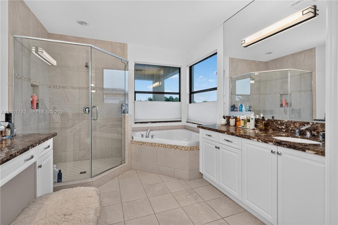 Bathroom featuring a double vanity with stone countertops, a corner soaking tub, and a glass-enclosed shower with tiled surround